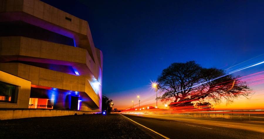 A Fundação Iberê ao anoitecer, com as luzes da avenida em rastros e o céu ainda azul
