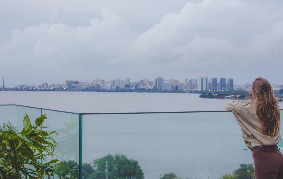 Mulher no alto olhando a cidade e o Guaíba, com as nuvens sobre a água