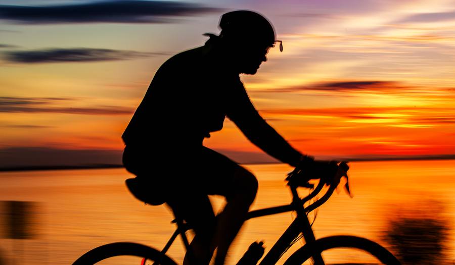 Ciclista em silhueta cruzando a orla no pôr do sol alaranjado