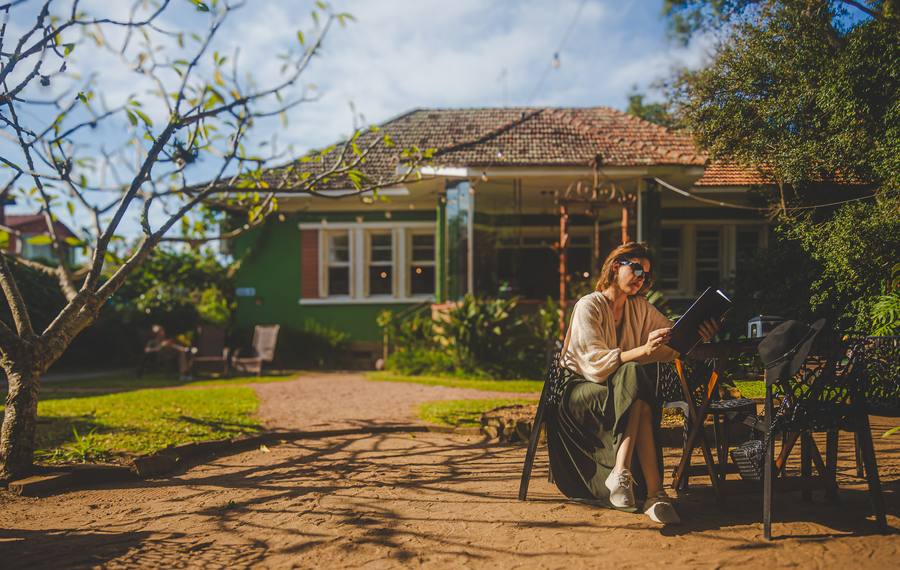 Mulher lendo em um banco no jardim de uma casa antiga