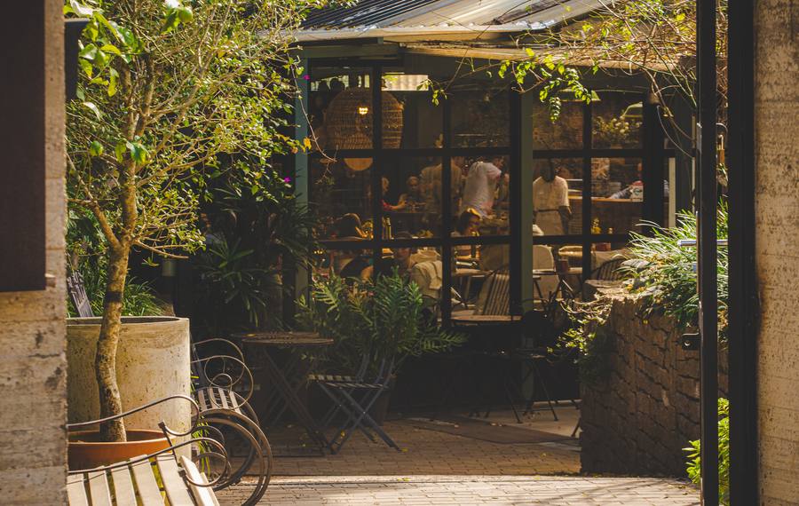 Café com mesas na calçada e plantas na entrada